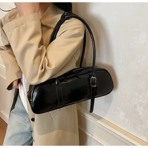 Detail of glossy black baguette bag with adjustable straps on trench coat model