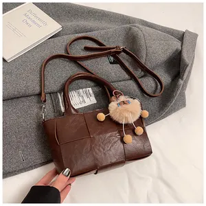 Vue détaillée du sac seau marron foncé tressé avec un joli pendentif en peluche