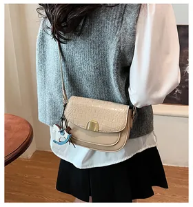 Detail of beige crocodile pattern saddle bag with gold buckle and a cute horse charm