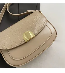 Macro shot of beige crocodile embossed saddle bag with elegant gold metal buckle lock