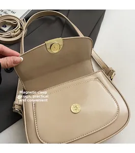 Detail of a beige crocodile-pattern saddle bag featuring a functional gold magnetic snap buckle