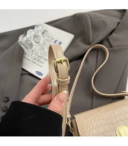 Close-up of adjustable strap with gold buckle on beige croc-embossed saddle bag