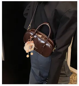 Detail of dark brown glossy leather crossbody bag with a cute plush sheep pendant