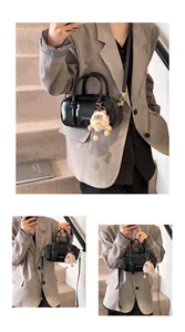 Detail of black minimalist handbag with gold logo and plush charm on a grey suit model