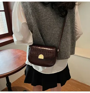 Detail of vintage reddish brown crocodile texture saddle bag with gold buckle hardware