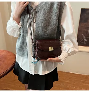 Detail of burgundy crocodile-textured leather saddle bag with gold buckle on model