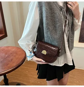 Detail of dark brown faux crocodile saddle bag with gold clasp and blue pony charm