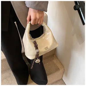Detail of cream white patent leather hobo bag with metal logo and woven bell pendant