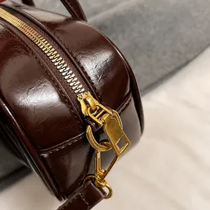 Close-up of golden zipper hardware and shiny brown leather texture of the square handbag