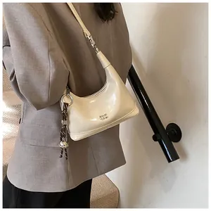 Detail view of cream patent leather hobo bag with bell charm and polished logo