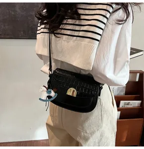 Detail of black crocodile texture saddle bag with gold buckle and a blue rocking horse charm
