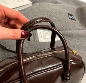 Close-up of gloss leather handbag with round handle and golden metal zipper detail