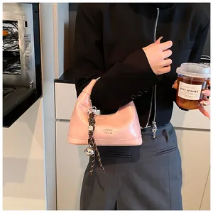 Pink patent leather hobo bag with woven charm detail held in a casual lifestyle setting