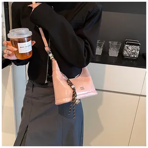 Pink glossy patent leather dumpling bag with woven tassel shown in a casual lifestyle setting