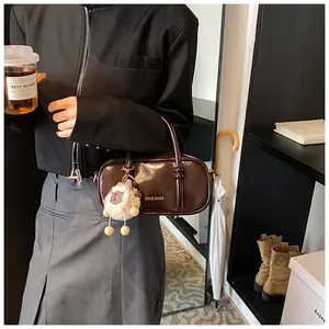 Detail of a dark brown glossy Boston bag with a plush doll charm held by a model