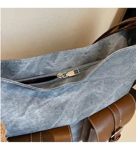 Close-up of smooth silver zipper and stitching on blue denim tote with brown leather