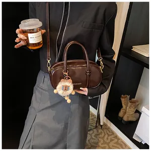 Detail of dark brown glossy leather crossbody bag with plush charm and knot handle design