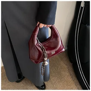 Detail of burgundy glossy leather handbag with woven rope and silver ball charm