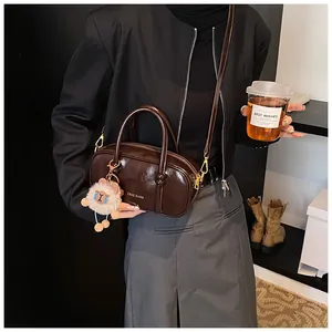 Detail of dark brown glossy leather handbag with a white plush alpaca charm and zip closure