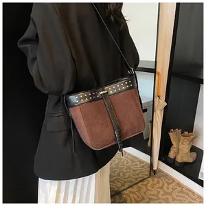 Detail of vintage suede messenger bag with rivets worn by a model in a studio setting