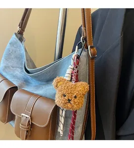 Detail of a brown plush bear keychain with a metal carabiner on a denim bag