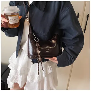 Detailed close-up of dark brown patent leather shoulder bag with woven pendant