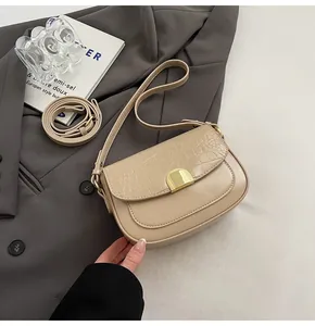 Close-up of beige saddle bag featuring crocodile pattern flap and golden metal buckle