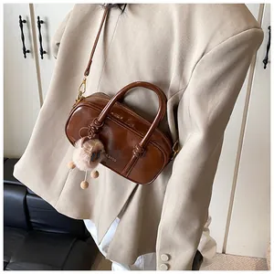 Detail of a deep brown shiny leather crossbody bag with fluffy charm on a model