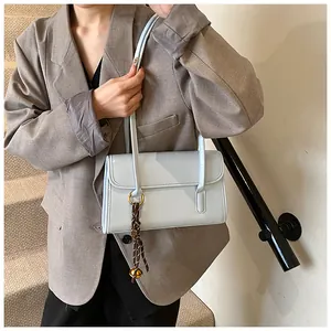 Detail of light blue faux leather shoulder bag with decorative brown woven strap charm