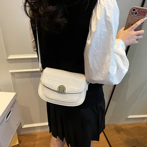 White faux leather saddle bag with crocodile texture and gold metal buckle worn by model