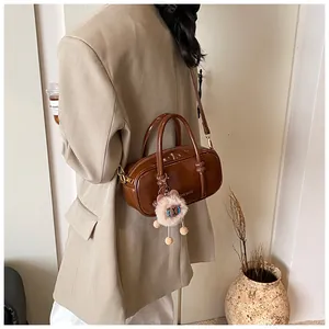 Detail of a brown gloss Boston bag with plush pendant and shoulder strap on model