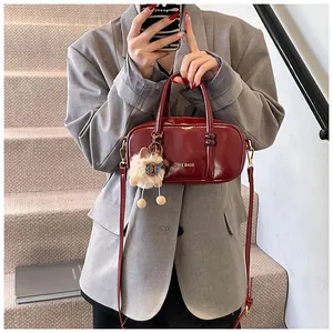Detail of burgundy patent leather handbag with dual handles and plush charm accessory