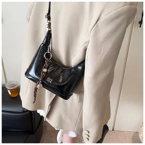 Detail of black glossy crescent bag with woven charm and branded white logo lettering