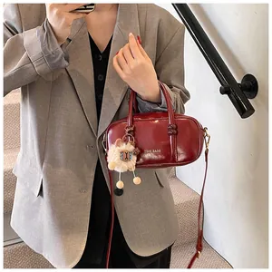 Fashionable burgundy leather Boston bag with plush charm on a casual shoulder strap