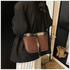 Close-up of brown suede crossbody bag with metal rivets and black leather strap detail