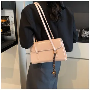 Lifestyle view of a beige glossy leather shoulder bag with a woven decorative charm