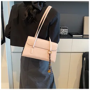 Side view of a glossy light pink shoulder bag with metallic ball charm on a model