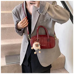 Detail of burgundy square handbag with gold logo, furry charm and detachable strap