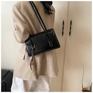 Detail of black faux leather shoulder bag featuring a woven tassel and small gold bell