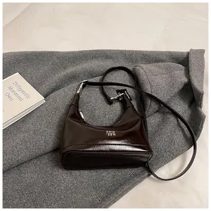 Detail of dark brown polished leather crescent bag with silver lettering on grey coat