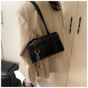 Detail of black glossy leather underarm bag with thin straps and a bell charm