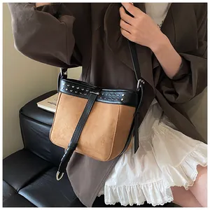 Detail view of brown suede crossbody bucket bag featuring silver rivets and black leather trim