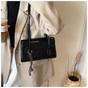 Detail of glossy black patent leather underarm bag with unique braided rope charm
