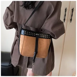 Detail shot of brown suede bucket bag with black leather trim and silver studs on strap