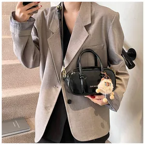 Urban chic black patent leather mini Boston bag with plush pendant on a model
