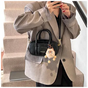 Detail of a chic black glossy mini square bag with a plush bear charm and crossbody strap