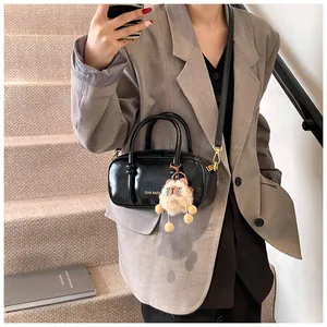 Detail of black patent leather square bag with gold hardware and plush charm on a strap