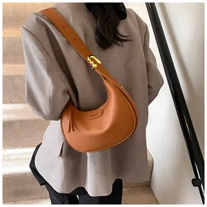 Dettaglio borsa a mezzaluna in pelle marrone con fibbia dorata e logo impresso