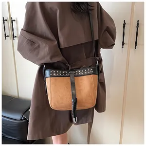 Detail of brown suede bucket bag with black leather trim and silver studs on trench coat
