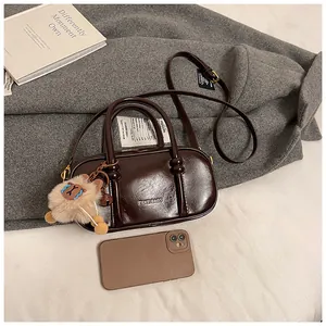 Close-up of glossy brown crossbody bag with metal logo and cute plush sheep charm